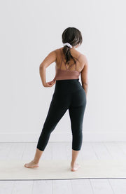 Back of woman standing on yoga mat wearing black crop leggings